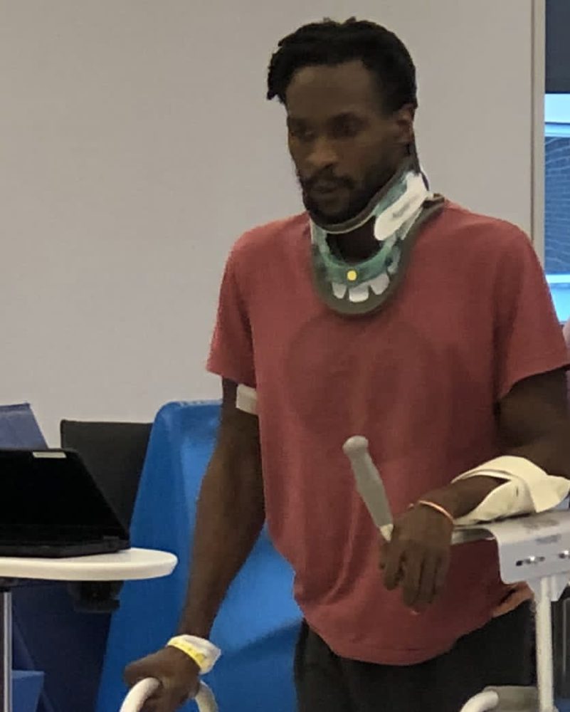 Keith Simmonds Jr. in a neck brace, standing with a walker during rehab after spinal cord surgery